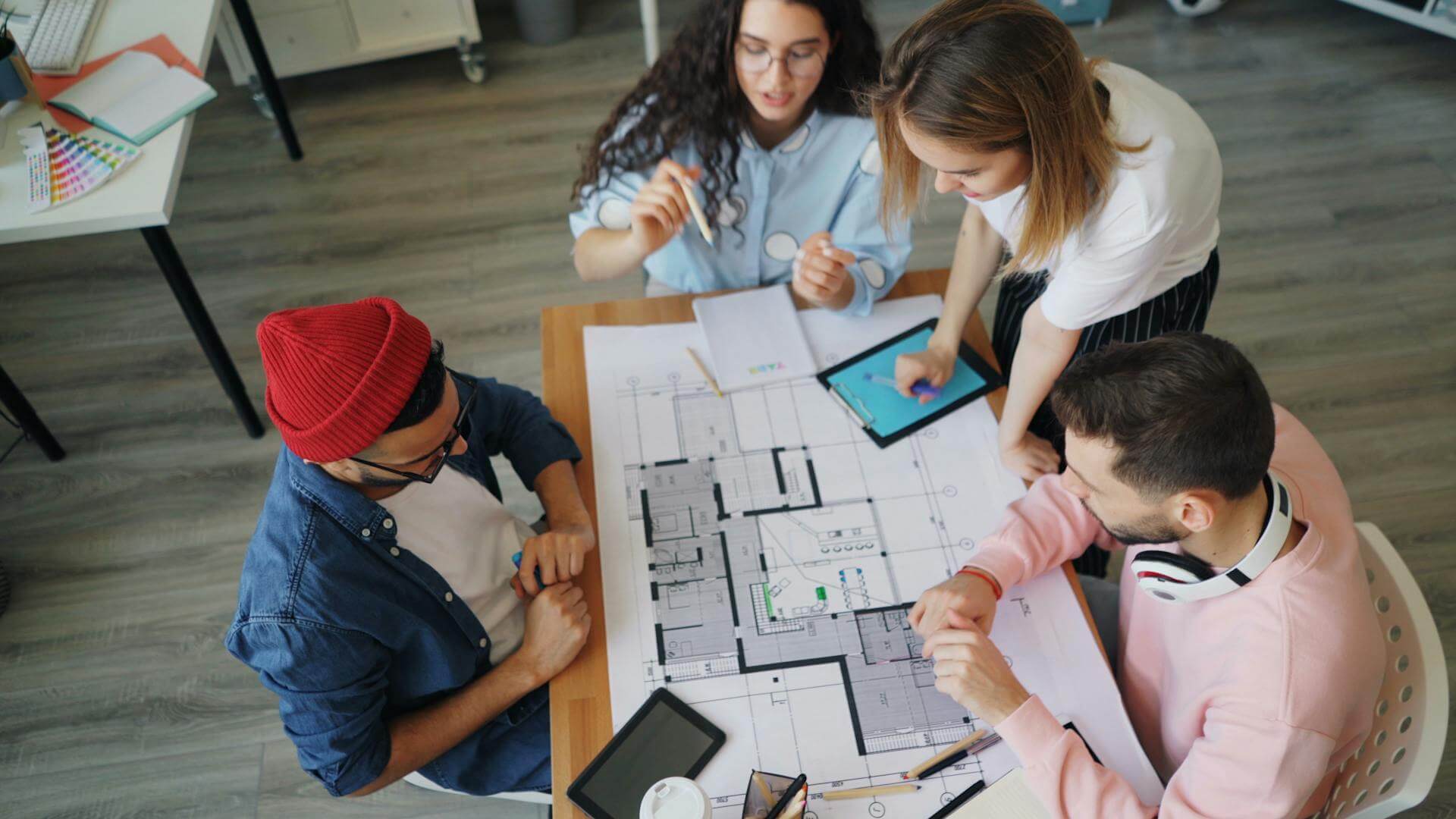 Four people sitting around a table looking at blueprints (Source: Pexels - Vitaly Gariev)